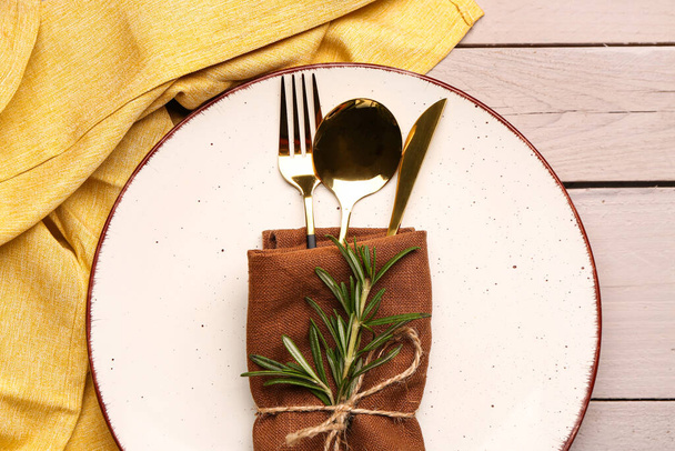 Plate with napkin, set of cutlery and rosemary on white wooden background - 写真・画像
