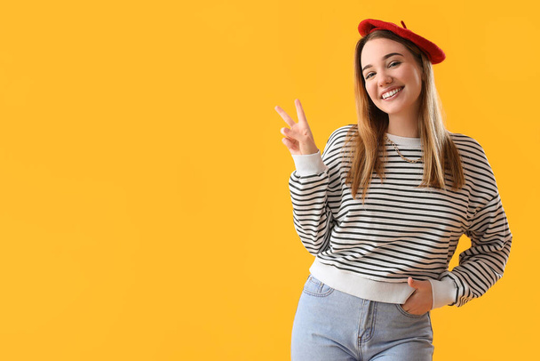 Young woman showing victory gesture on yellow background - Foto, afbeelding