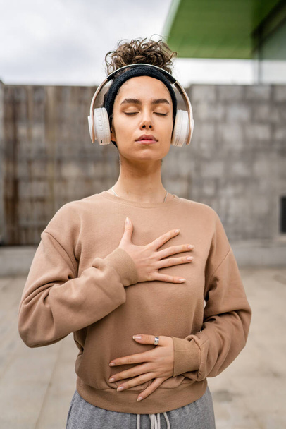 eine erwachsene kaukasische Frau mit Kopfhörern für online geführte Meditation praktiziert Achtsamkeit Manifestation mit geschlossenen Augen stehen im Freien echte Menschen Selbstpflege-Konzept kopieren Raum - Foto, Bild