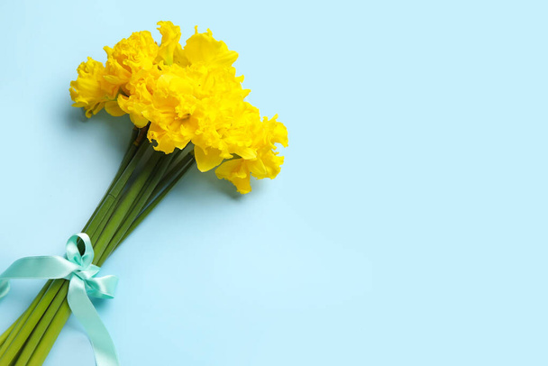 Beautiful narcissus flowers with blue ribbon on color background - Фото, зображення
