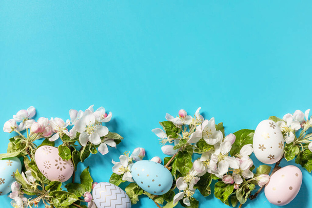 Húsvéti kompozíció színes tojásokkal és almafa virágokkal, kék háttérrel. Tavaszi fogalom, virágkompozíció. Üdvözlőlap. Kilátás fentről. Fénymásolási hely. - Fotó, kép