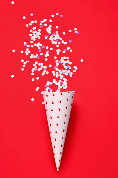 Cône de fête avec confettis sur fond rouge - Photo, image