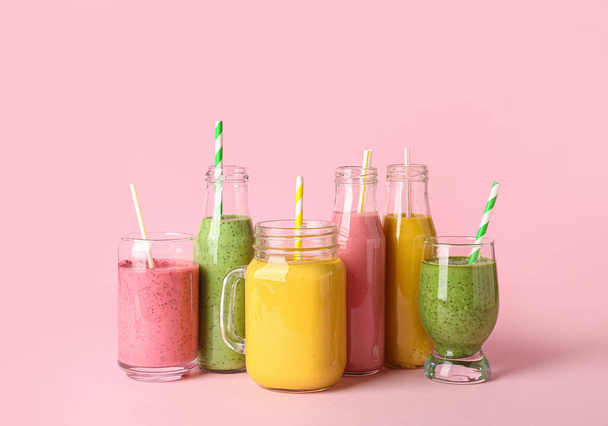 Glasses and bottles of different tasty smoothie with straws on pink background - Foto, Imagem