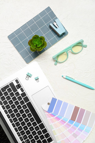 Composition avec ordinateur portable, lunettes, bloc-notes et plante sur fond blanc - Photo, image