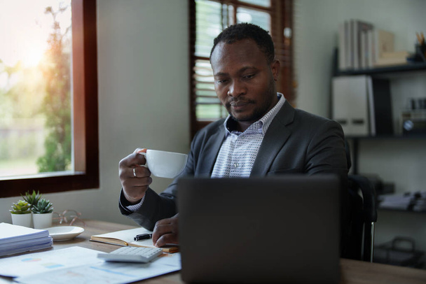 hombre de mediana edad americano africano utilizando ordenador portátil con la planificación de trabajo en documentos financieros, impuestos, intercambio, contabilidad y asesor financiero. - Foto, Imagen