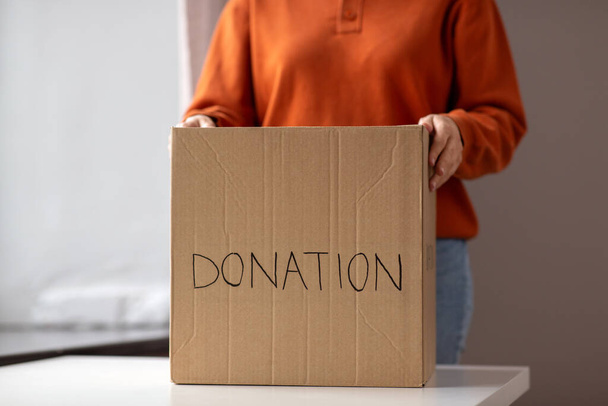 charity and volunteering concept - young woman holding cardboard box with donations at home - Zdjęcie, obraz