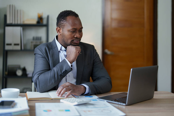 mężczyzna w średnim wieku American African za pomocą laptopa komputerowego z planowaniem pracy nad dokumentem finansowym, podatki, wymiana, księgowość i doradca finansowy. koncepcje biegłego rewidenta lub rewidenta. - Zdjęcie, obraz