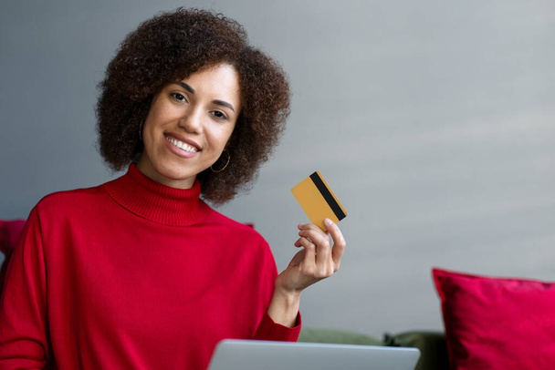 Mosolygó afro-amerikai üzletasszony kezében hitelkártya laptoppal, online vásárlás, rendelés élelmiszer a honlapon. Boldog magabiztos szabadúszó kap fizetséget. Technológia, sikeres üzleti koncepció - Fotó, kép