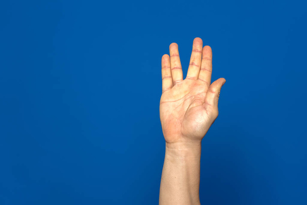 Lenguaje de signos americano. Mano masculina mostrando la letra V hecha con cuatro de sus dedos aislados sobre fondo azul. - Foto, Imagen