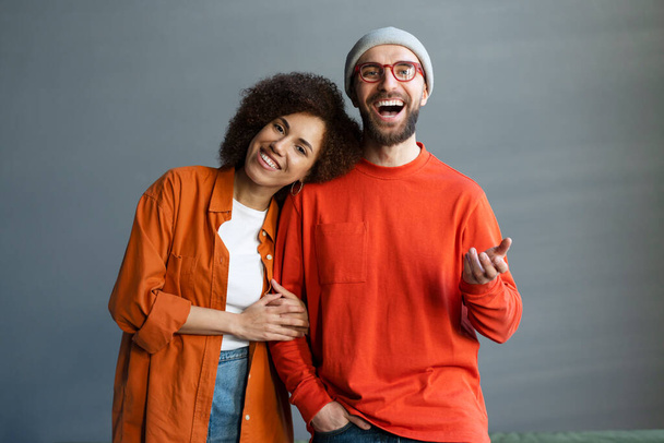 Szczęśliwa stylowa atrakcyjna para przyjaciół obejmująca, stojąca razem w domu. Portret młodej uśmiechniętej koleżanki z pracy ubranej w kolorowe ubrania patrzącej w kamerę. Sprawy zakończone powodzeniem - Zdjęcie, obraz
