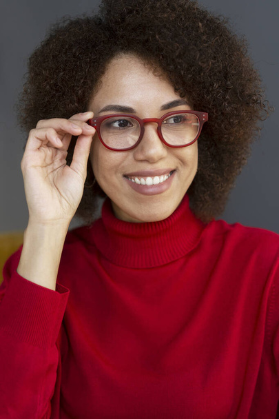 Портрет, який посміхається афро-американській жінці в стильних червоних окулярах і червоному светрі з білизною, виглядає ізольованим на задньому плані. Концепція зору - Фото, зображення