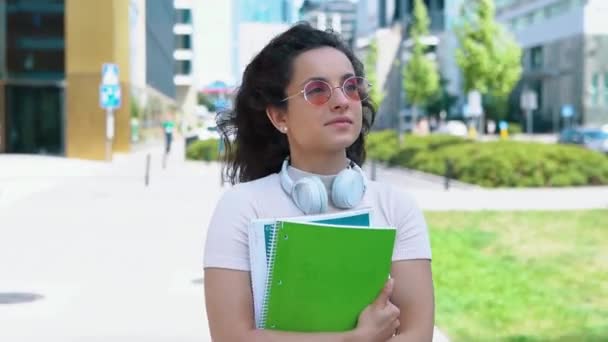 Счастливая студентка собирается на лекцию. Улыбающаяся женщина в солнечных очках с книгами и блокнотами. Концепция образования. В реальном времени - Кадры, видео