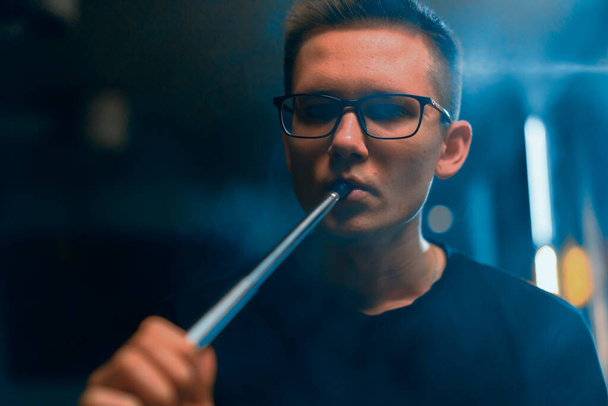 Hookah άνθρωπος με γυαλιά καπνίζοντας μια παραδοσιακή πίπα Hookah Ο άνθρωπος εκπνέει καπνό σε hookah cafe ή lounge bar - Φωτογραφία, εικόνα