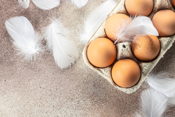 brown chicken eggs with feathers. in an open egg carton on light background. top view, - Фото, изображение