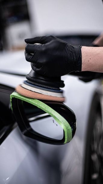 Mitarbeiter eines Autohauses oder einer Waschanlage poliert den Lack eines schwarzen Autos am Rückspiegel - Foto, Bild