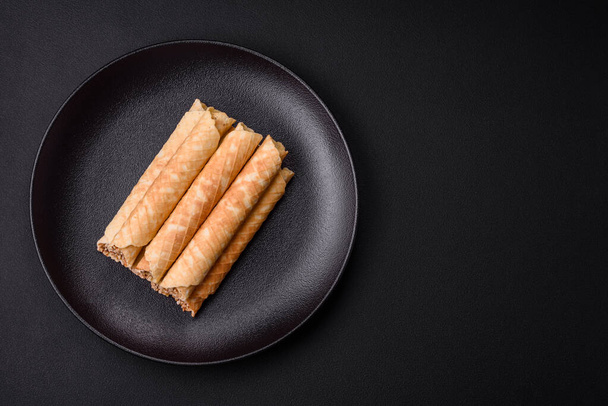 Delicious crispy wafer rolls with cream filling with nuts on a dark concrete background - Foto, Imagen