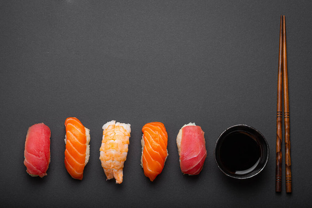 Traditional Japanese sushi top view with soy sauce and chopsticks on dark black minimal background. Sushi with salmon, tuna and shrimp, space for text - Фото, зображення