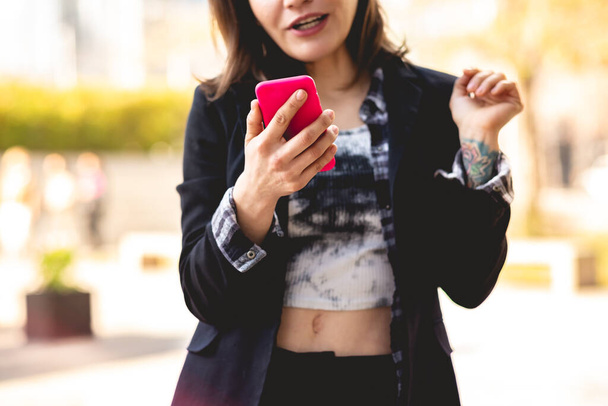 Moderní a mladý manažer: krásná a sofistikovaná žena kontroluje jeho růžový telefon v městském parku - Fotografie, Obrázek