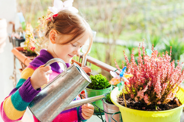Adorable little girl watering plants on the balcony on a nice sunny day - Фото, изображение
