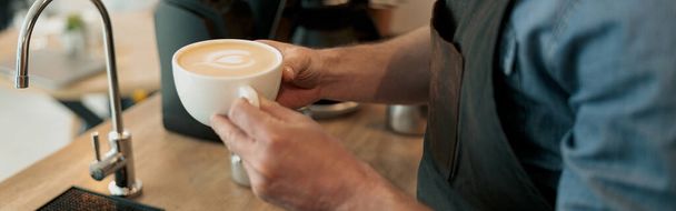 Close up of man hands standing by wooden table with cup of cappuccino - 写真・画像