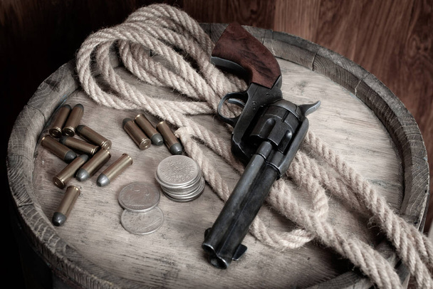 Old west revolver with cartridges and silver dollar coins on wooden barrel - Foto, Imagem