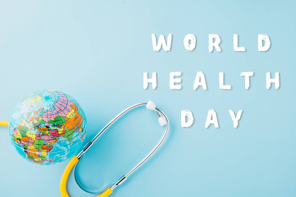 World Health Day. Top view yellow doctor stethoscope wrapped around world globe isolated on pastel blue background with copy space for text, Save world day, Health care and medical concept - Zdjęcie, obraz
