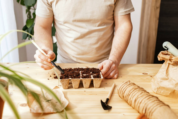 The process of planting seeds. A man pours earth with a small spatula into ecological peat moulds. Landscaping and gardening in the apartment.  - Photo, Image