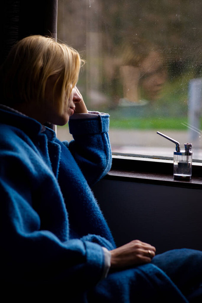 A woman is sitting near the window with a device for smoking marijuna. Relaxation with cannabis. Medicinal cannabis. - Φωτογραφία, εικόνα