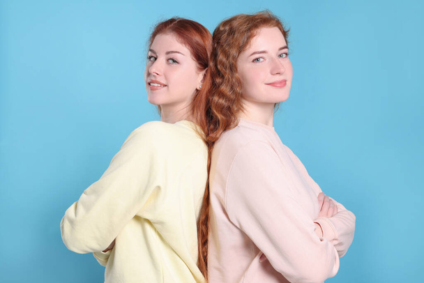 Portrait of beautiful young redhead sisters on light blue background - Fotoğraf, Görsel