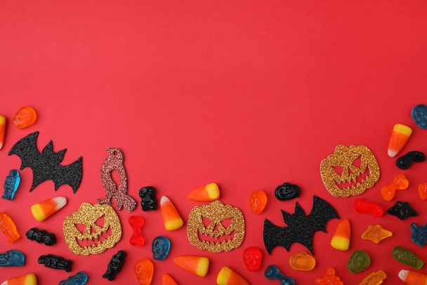 Tasty candies and Halloween decorations on red background, flat lay. Space for text - Photo, Image
