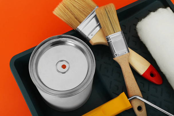 Can of orange paint, brushes, roller and container on color background, closeup - Foto, Imagem
