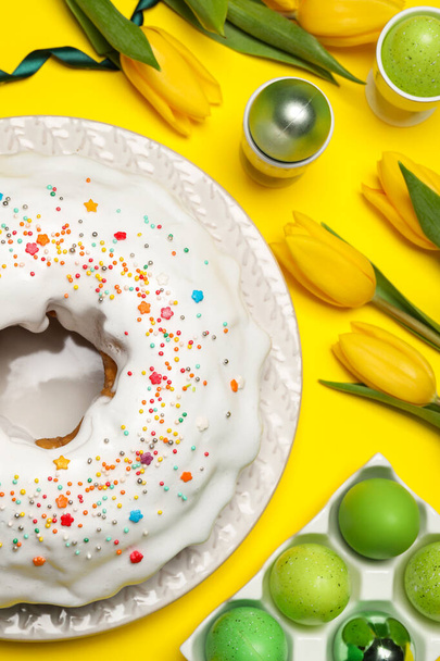 Easter cake with sprinkles, painted eggs and tulips on yellow background, flat lay - Photo, Image