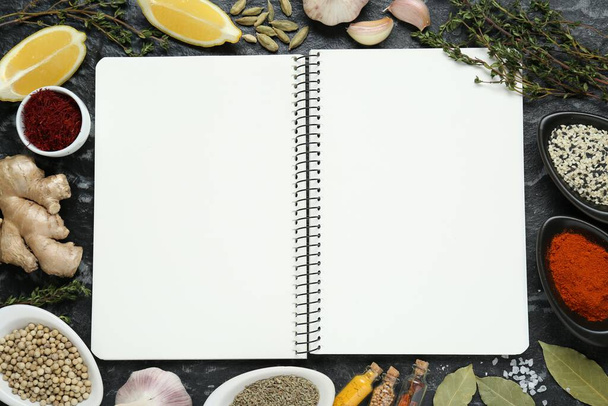 Blank recipe book surrounded by different ingredients on black textured table, flat lay. Space for text - Φωτογραφία, εικόνα