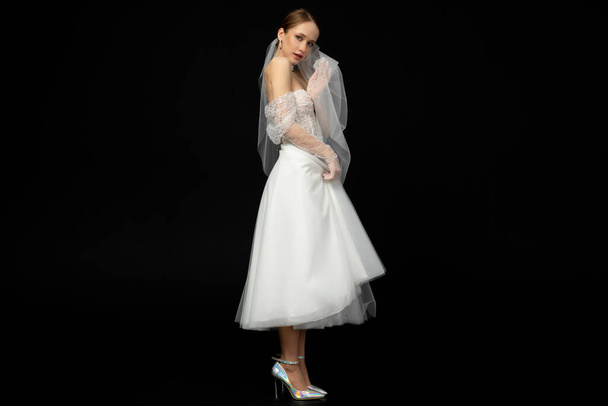 Nahaufnahme Porträt eines schönen charmanten Mädchens, die Braut in einem luxuriösen und eleganten weißen Hochzeitskleid, posiert und gestikuliert zärtlich mit einem Schleier in den Händen. Vereinzelt auf schwarzem Hintergrund. - Foto, Bild