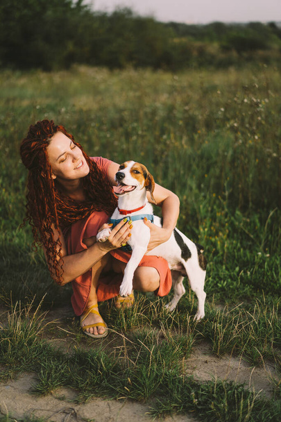 Mooie vrouw speelt met haar Jack Russell hond in het park. Het concept van dieren, vriendschap, mensen en liefde. een vrouw ligt op het gras en speelt met een boer russell terrier - Foto, afbeelding