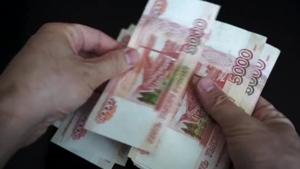 Adam elinde bir paket Rus rublesi ve yaprağı tutuyor. Rus 5000 banknot ellerinde. Adam maaşı yeniden hesaplıyor. İşadamı siyah bir arkaplanda gelir düşünüyor - Video, Çekim