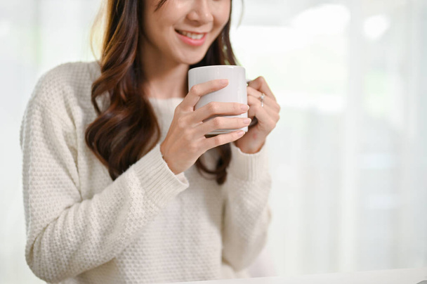 Image en gros plan d'une belle et détendue jeune femme asiatique prenant son café du matin dans le salon. - Photo, image