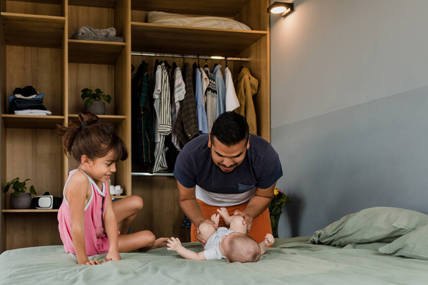 小さな赤ちゃんを持つ若いラテン系の父は、メキシコの自宅でおむつを交換しながらラテンアメリカ、ヒスパニック系の家族 - 写真・画像