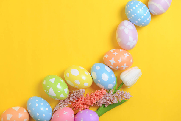 Mutlu Paskalya bayramı tebrik kartı konsepti. Sarı arka planda renkli Paskalya yumurtaları ve bahar çiçekleri. Üst görünüm, düz görünüm, kopyalama alanı. - Fotoğraf, Görsel