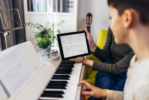 Brother and sister play electric piano at home and have fun. The sister helps her younger brother to play piano.They use a digital tablet for online lessons. - Fotoğraf, Görsel