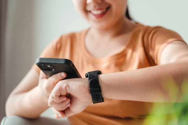 young woman looking and using a smartwatch, Female sitting on the sofa checking her smartwatch. - Photo, Image