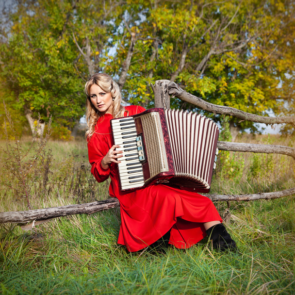 Retro vrouw in klederdracht met een accordeon, in een veld - Foto, afbeelding