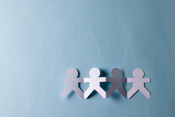Close up of four paper cut out people figures holding hands with copy space on blue background. Humanitarian, people, help and human concept. - Photo, Image