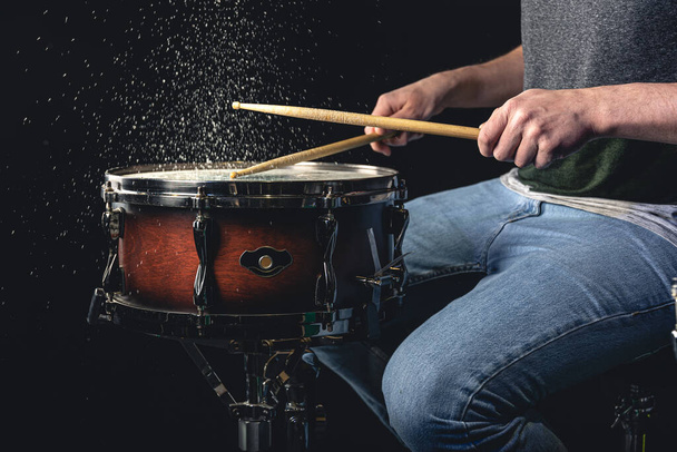 Schlagzeuger mit Schlagstöcken schlägt Snare Drum mit Spritzwasser auf schwarzem Hintergrund. - Foto, Bild