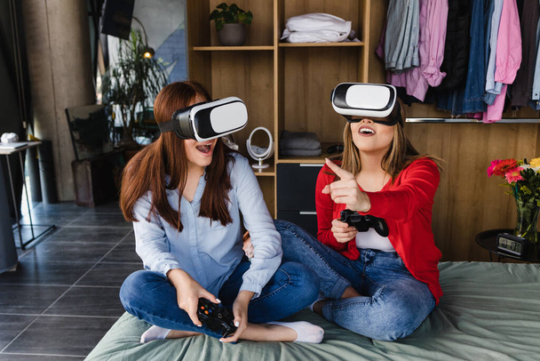 latin couple of women playing virtual reality video games on bed in their home together in Mexico Latin America, hispanic people - Foto, Bild