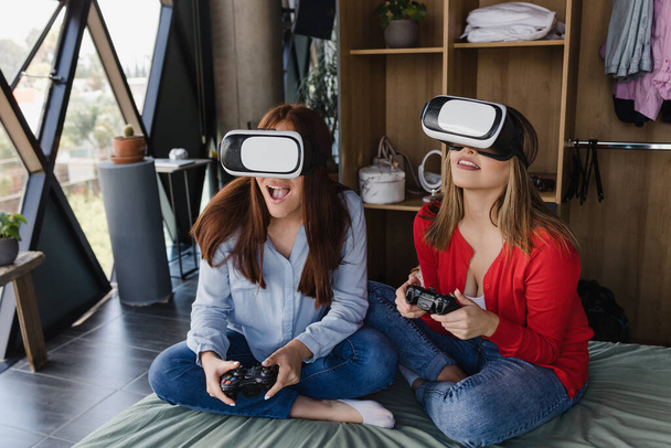 lateinisches Paar von Frauen, die Virtual-Reality-Videospiele auf dem Bett in ihrem Haus in Mexiko Lateinamerika spielen, hispanische Menschen - Foto, Bild