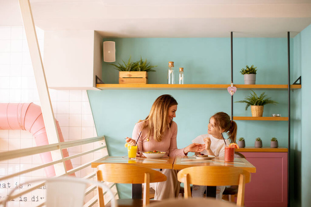 Mother and daughter having good time during breakfast with fresh squeezed juices in the cafe - Photo, Image