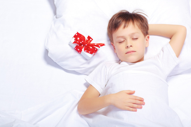 Πορτρέτο του μικρού αγοριού στο κρεβάτι με ένα δώρο - Φωτογραφία, εικόνα