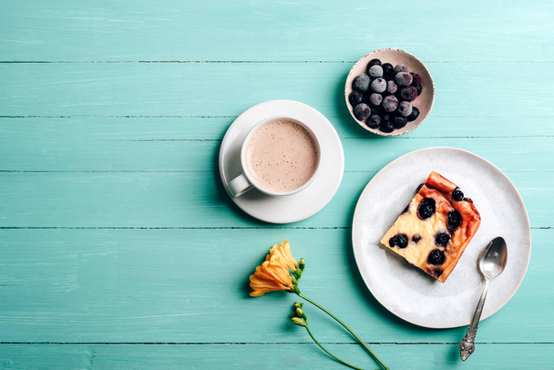 Une tasse de gâteau au café et aux myrtilles, fleur de freesia jaune sur fond de bois turquoise. Vue du dessus, plan, espace de copie. - Photo, image