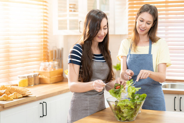 glücklich und lächelnd lesbisches Paar, das in der Küche Salat kocht. Salat in Glasschüssel mit süßem Lächeln beim gemeinsamen Kochen. Stolzer Monat zur Förderung von Gleichberechtigung und Unterschieden zwischen Homosexuellen. - Foto, Bild